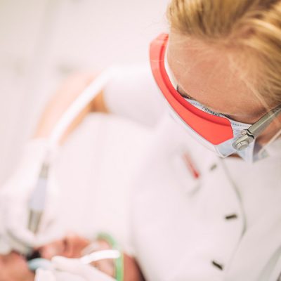 Mitarbeiterin mit Mundschutz und Brille reinigt die Zähne von Patienten professionell