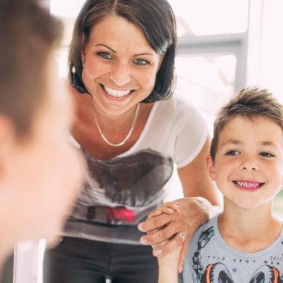 Mutter hält Jungen an der Hand, dessen Zähne angefärbt wurden