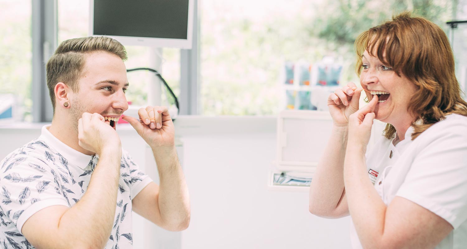 Mitarbeiterin zeigt Patienten Reinigung mit Zahnseide