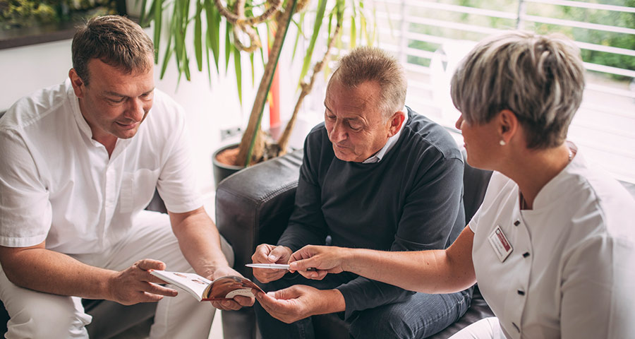 Dr. Andreas Pohl und Mitarbeiterin erklären Patienten die Behandlungsmethode All-on-4